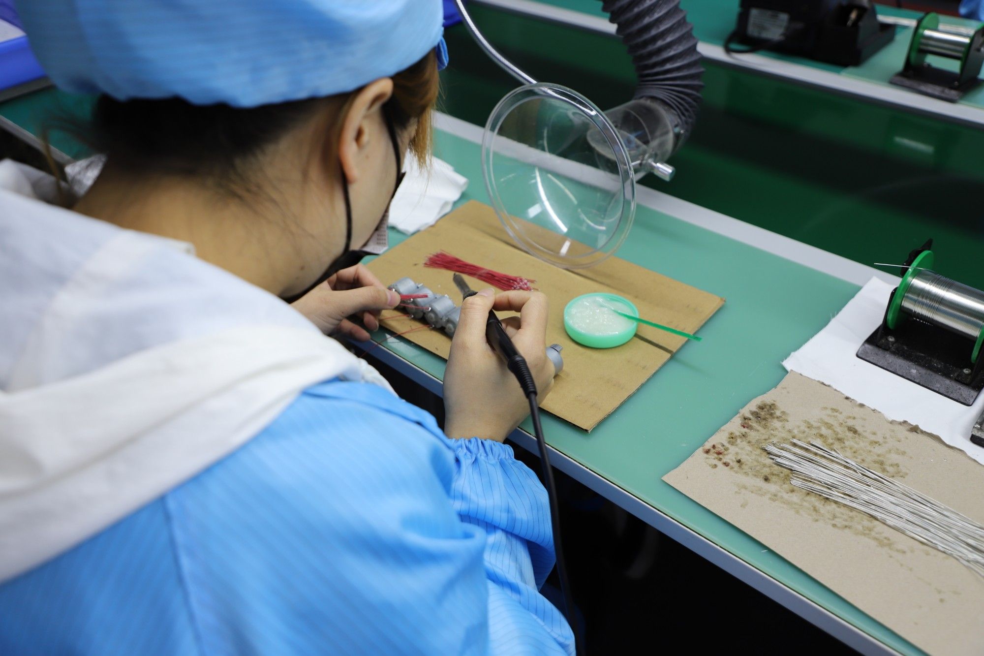 Technician soldering lead wires to vibration motors at a fume-extracted bench before silicone encapsulation