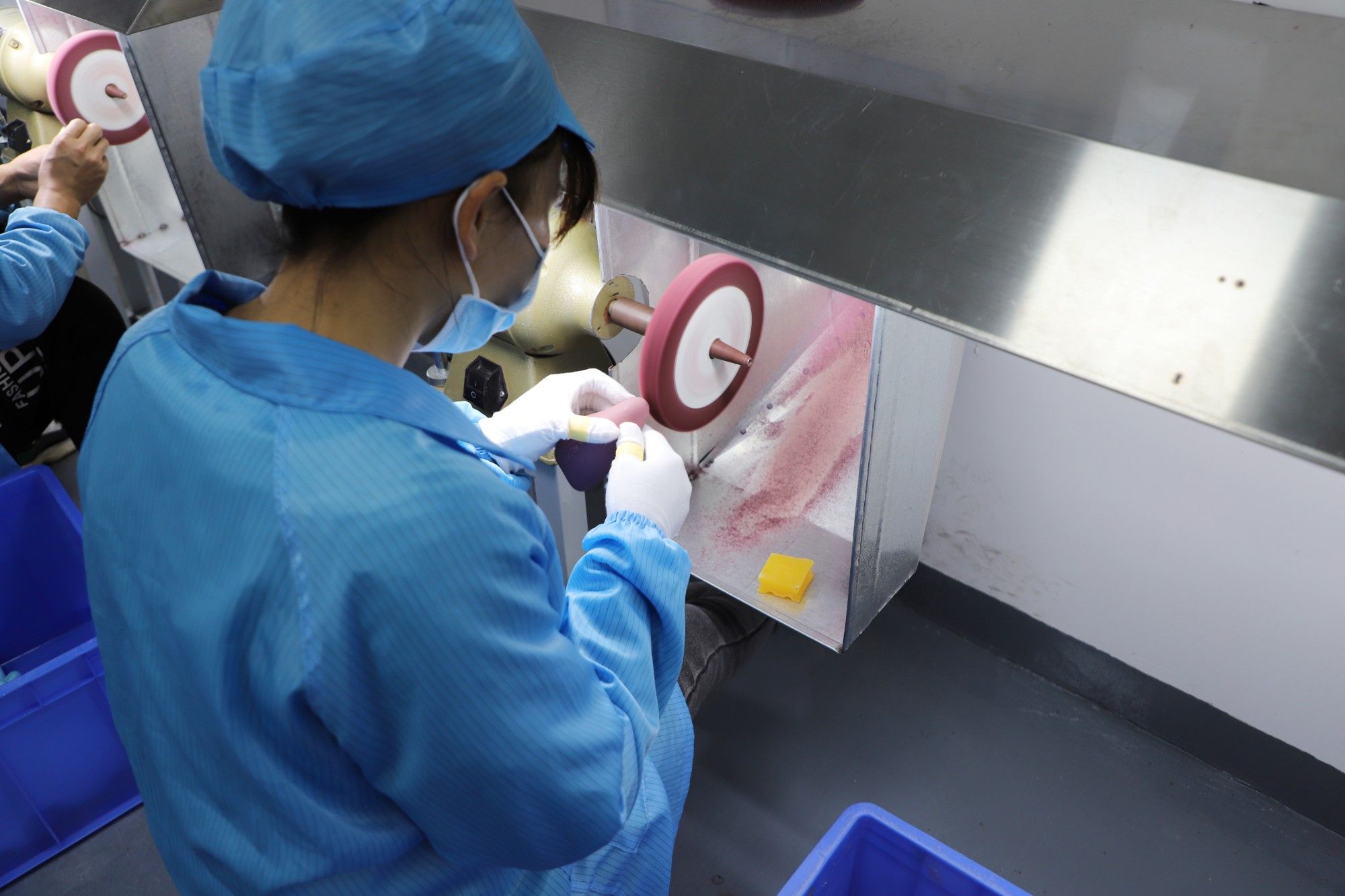Operator in cleanroom gown hand-polishing a molded silicone part at an extraction-hooded polishing wheel