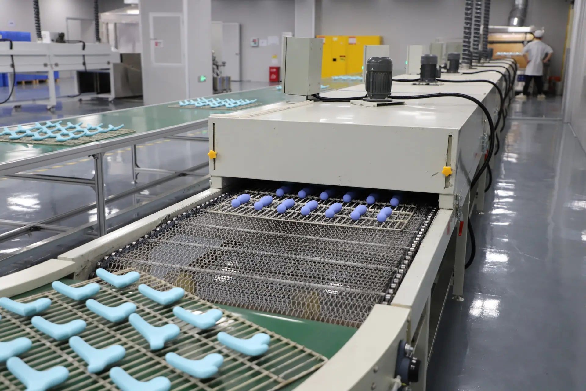 Oil-spray-coated silicone parts on a mesh conveyor entering Leutoo's tunnel curing oven