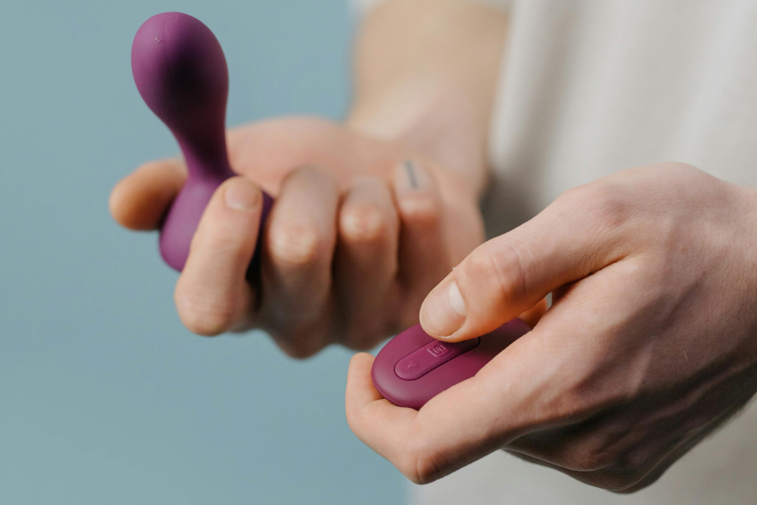 A person holding a purple personal massager and remote with a muted background.